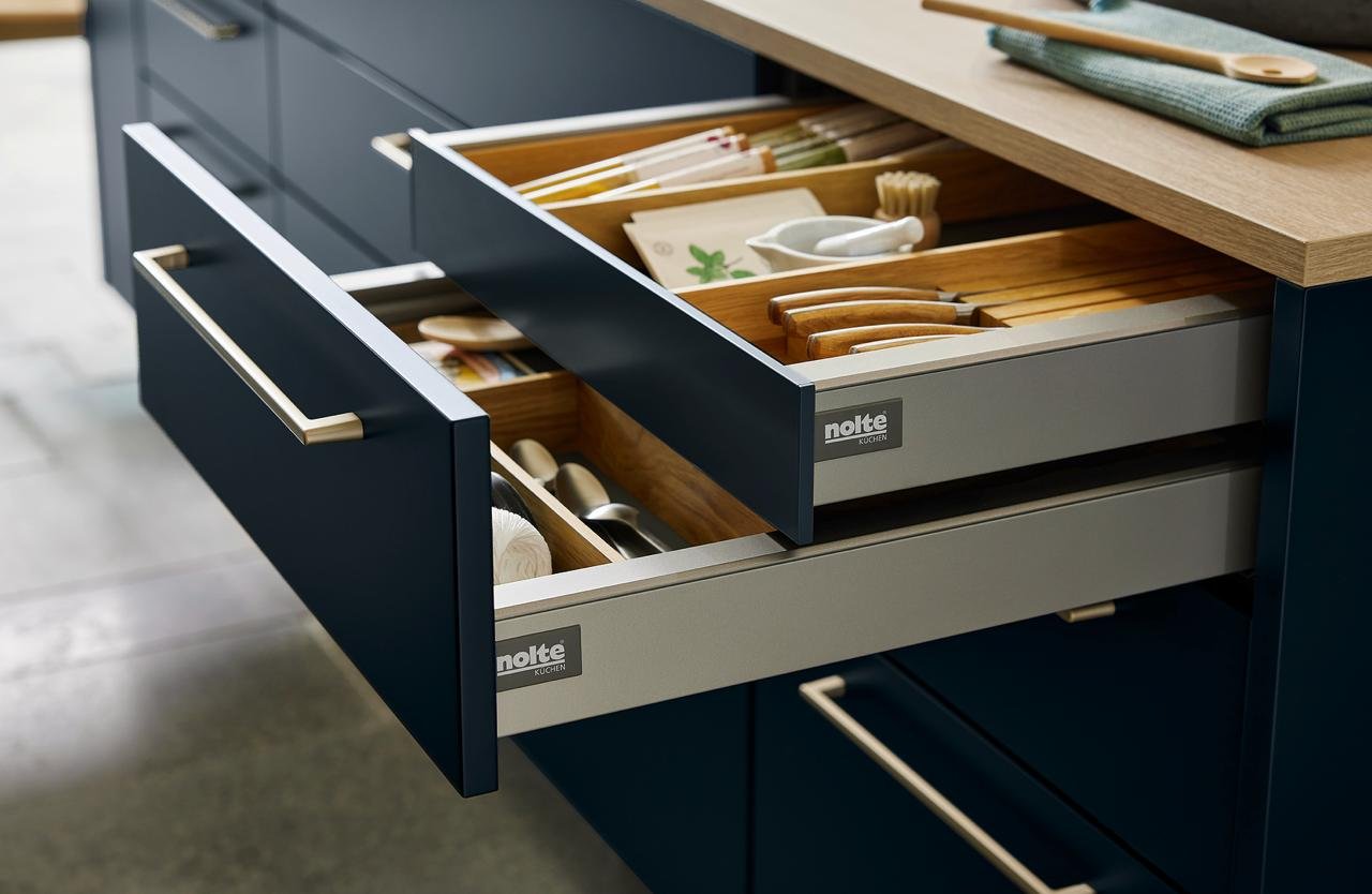 Open Nolte-branded drawer with cutlery organiser in a navy kitchen